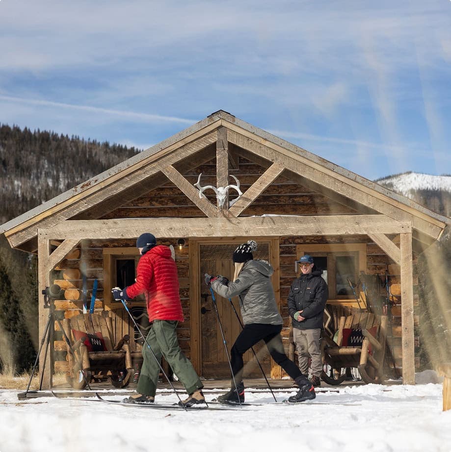 people walking in skis in front of a cabin