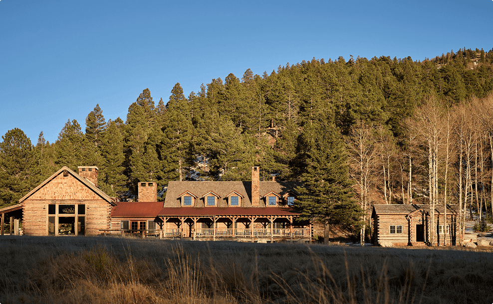 Rustic lodge-style residence surrounded by trees at the base of a forested hillside.