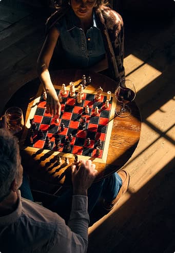 Two people playing chess at a small table with drinks nearby.