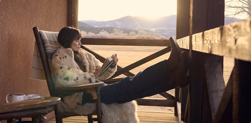 Person relaxing on a porch chair reading with mountain views at sunset.