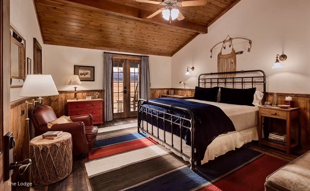 Rustic lodge bedroom with wood accents, metal bed frame, and mountain view through glass doors.