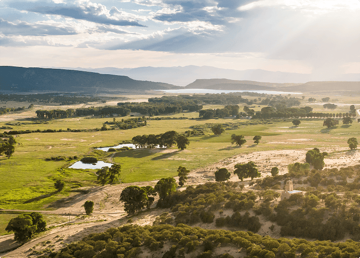 Aerial view of a scenic valley with river, trees, and sunlight breaking through clouds.