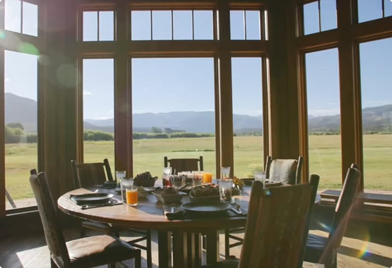 Breakfast table set inside a lodge with large windows overlooking open fields and distant mountains.
