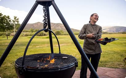 Chef preparing a gourmet outdoor dining experience beside an open-fire grill with mountain views at Trinchera Reserve & Lodge.